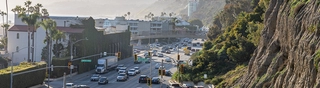 view of highway with cars, left side has buildings, right side is mountains